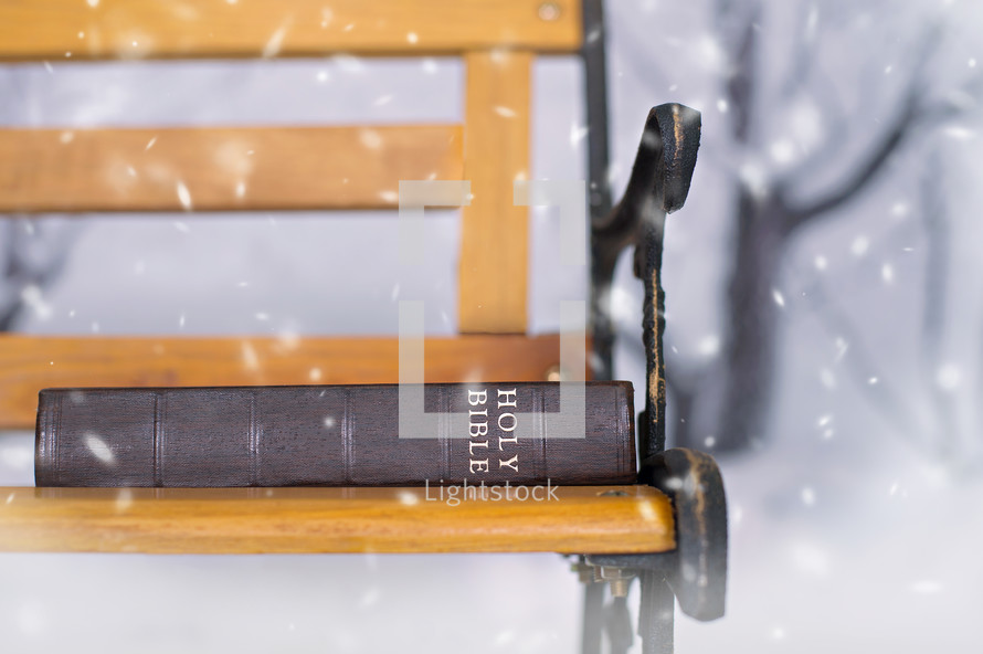 a Bible sitting on a park bench in the snow 
