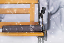 a Bible sitting on a park bench in the snow 