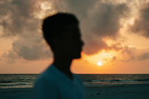 silhouette of a young man standing on a beach at sunset 