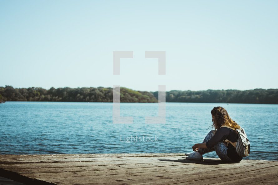 a young woman sitting alone on a dock 