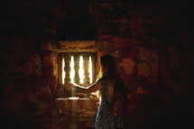 a woman standing in sunlight through an old window in an ancient cellar 