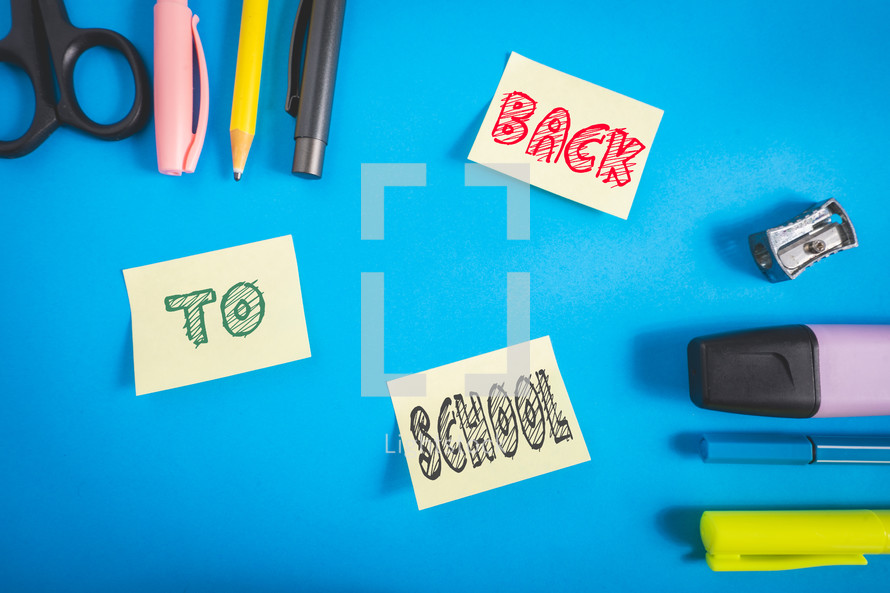 Office and school supplies on a blue background. And three sticky notes with back to school on it.