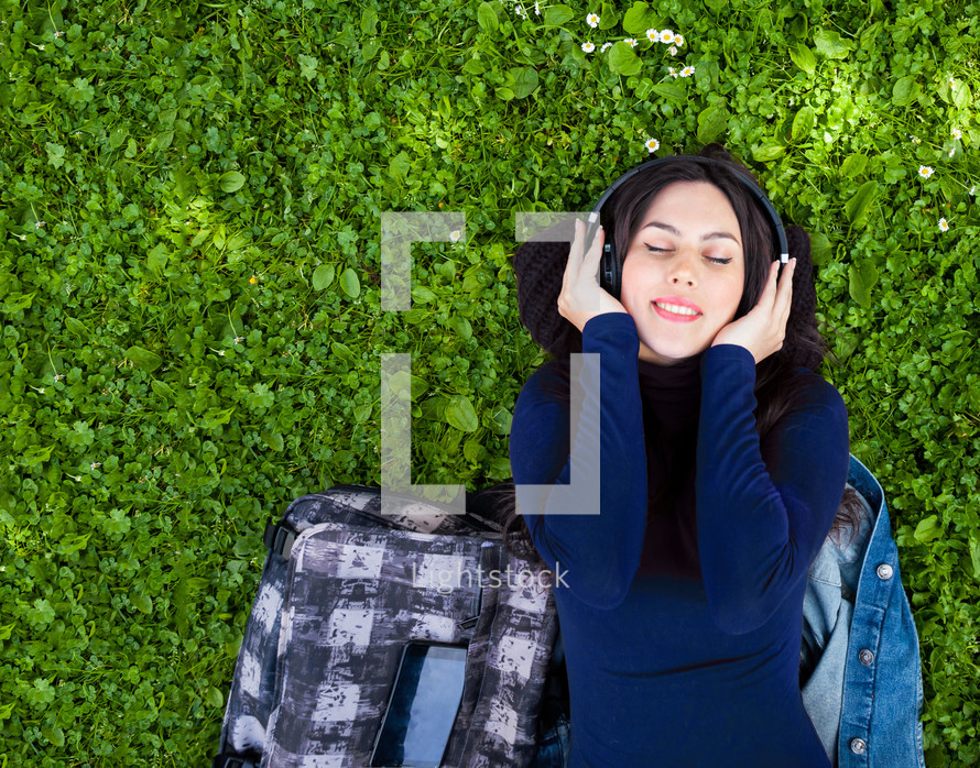 Portrait of cute young woman listening music with headphones in outdoor. Copy space on the green grass.
