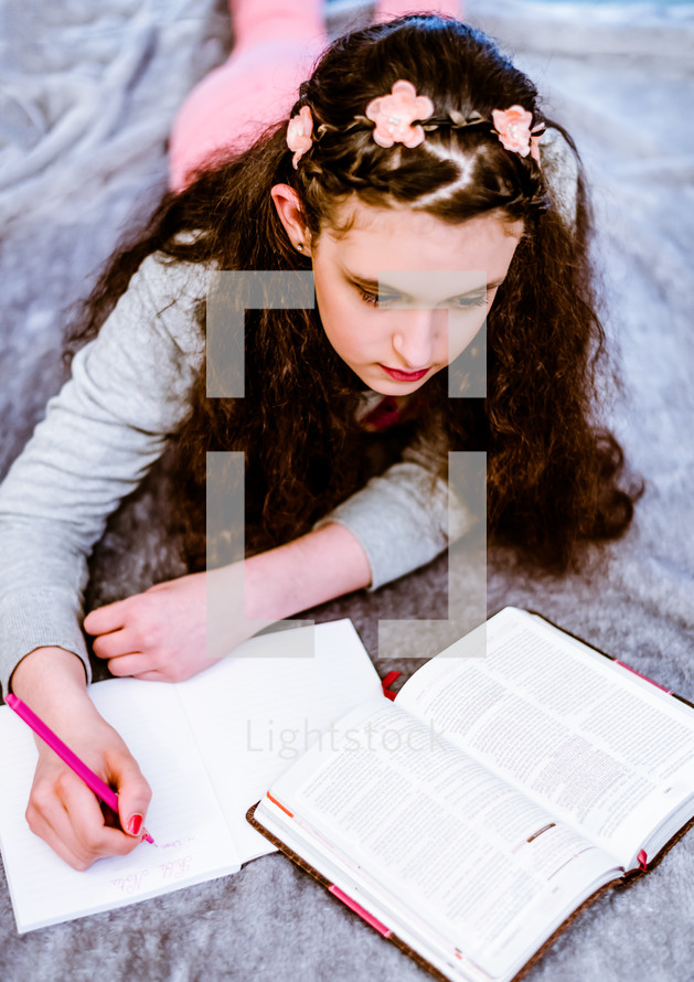 teen girl reading a Bible and writing in a journal 
