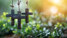 Three wooden crosses hanging in a garden with a blurred background.