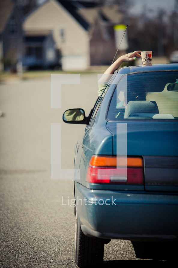 woman reaching for a coffee cup that she left on her car roof
