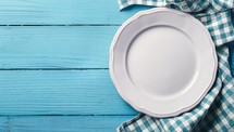 Empty plate and napkin on blue wooden background. Top view with copy space
