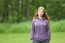 a teen girl in a hoodie standing outdoors 