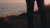 Man standing at cliff overlooking ocean during sunset