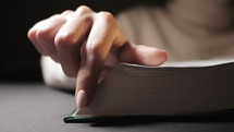 Close up of a woman's hands as she plays with the edges of Bible pages.