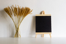 vase of brown fuzzy grasses and blank easel 