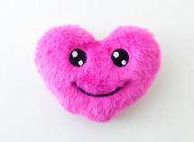 Pink fluffy heart toy smiling against a white background