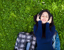 Portrait of cute young woman listening music with headphones in outdoor. Copy space on the green grass.