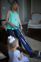 a woman vacuuming while her toddler daughter watches tv 