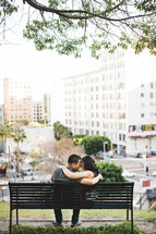 man and woman sitting on a park bench with their arms around each other