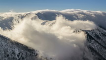 Time lapse of snowy, winter mountains with low clouds flying over ridge in morning light
