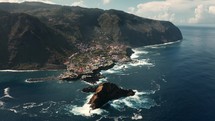 Sea mountain village in Madeira Portugal, aerial view of waves crashing and scenic clouds in the background