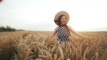  Cheerful woman in straw hat running in wheat golden field during sunset.