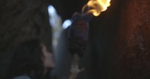Woman in a dark cave walking through a narrow corridor with a hand made torch