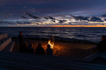 people sitting by a fire on a beach at sunset 