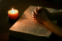 praying hands over the pages of a Bible and candlelight 