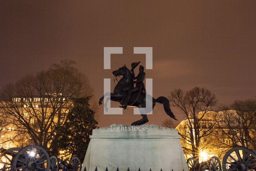 Bronze statue of Andrew Jackson on a horse, surrounded by cannons at night.