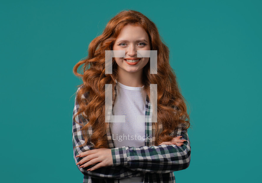 Pretty red long curly haired woman in hipster plaid shirt, natural beauty. Young girl on blue, charming eyes. American white appearance looking at camera. High quality 