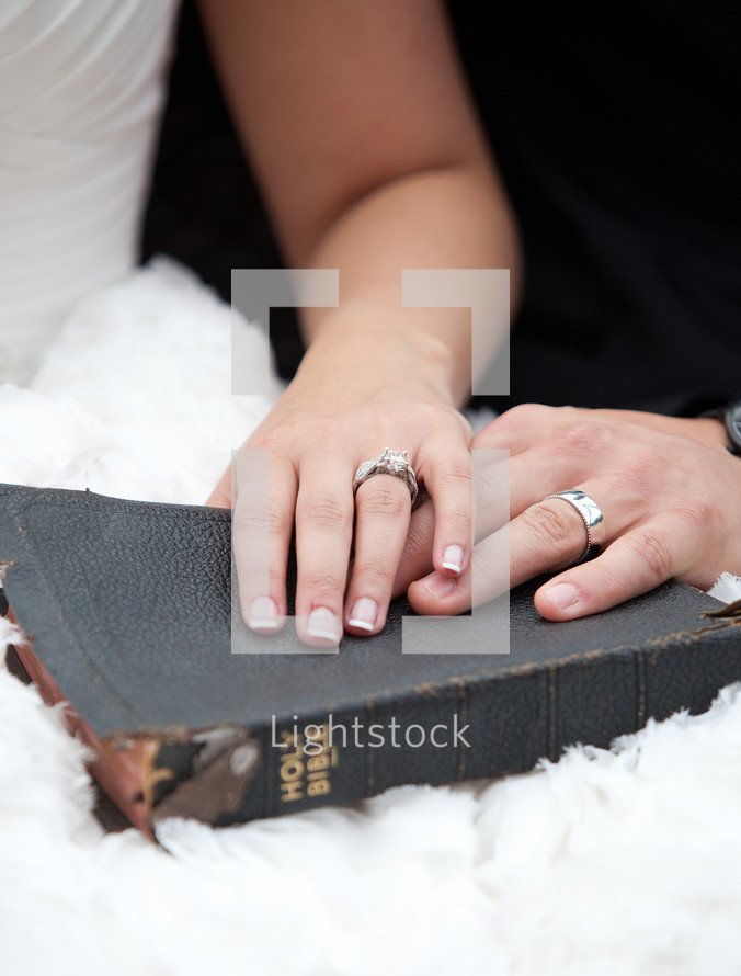 Husband and wife's hands on a tattered Bible.