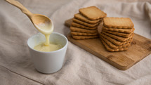 bowl with condensed milk with wooden spoon and biscuits in the background