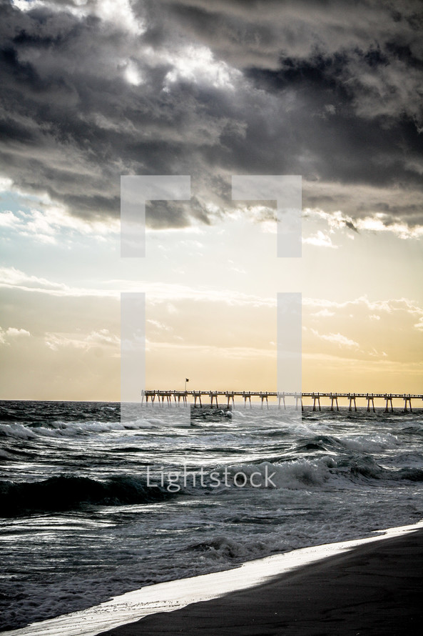 A long wooden pier extending into a stormy sea.