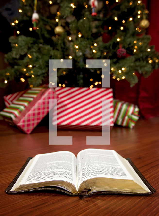 An open Bible on the floor in front of a decorated Christmas tree 
