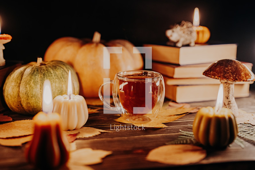 Glass cup of tea among pumpkin candles. Autumn-themed content, cafe promotions or visual storytelling that exudes comfort. Touch of intimacy, tranquil and inviting atmosphere. 