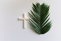 A wooden cross and a green palm leaf on a white background. Palm Sunday