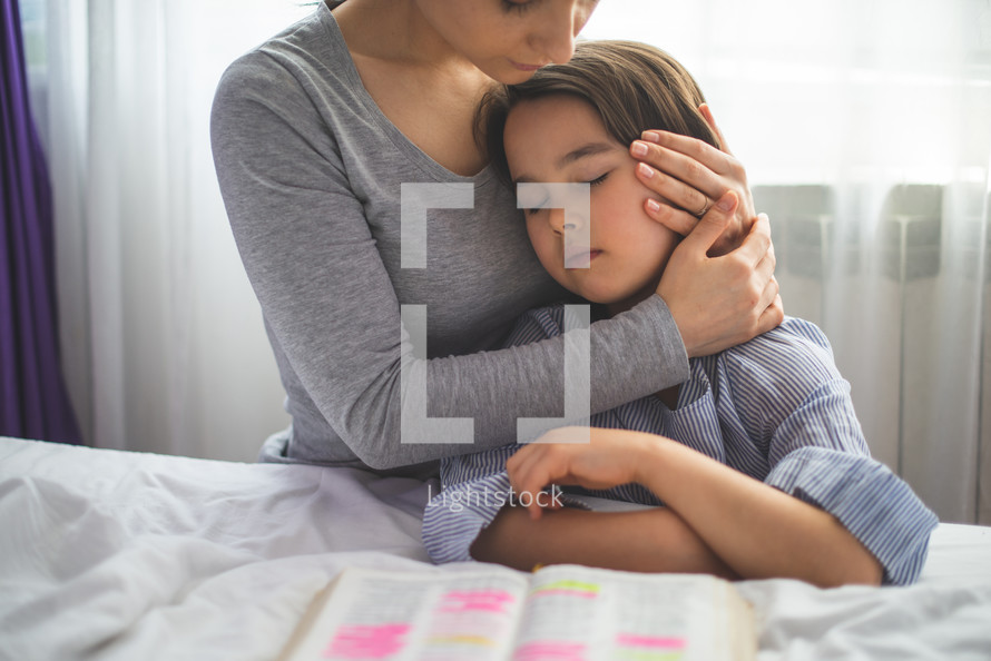 a mother hugging her child in front of an opened Bible 