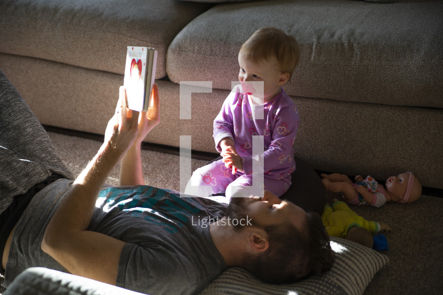 father reading a book to his toddler daughter 