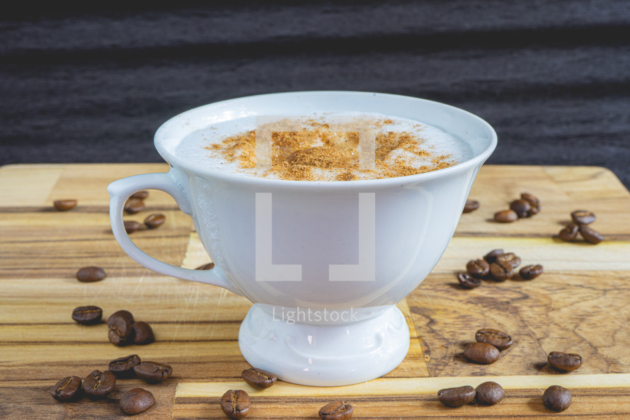 Delicious home made Cappuccino, in a white cup, on a wooden table. With coffee beans. Home made Coffee.