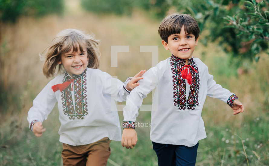 Little ukrainian boys cheerfully running along path in apple garden lawn. Children together in traditional embroidery vyshyvanka shirts. Ukraine, brothers, freedom, national costume, patriots.