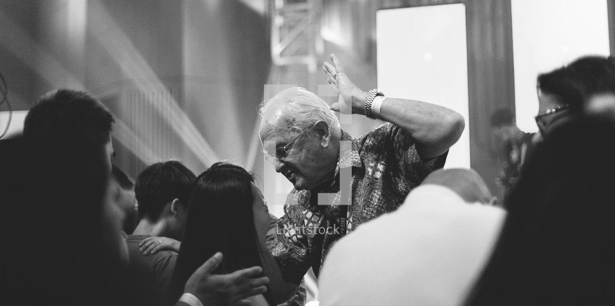 elderly man placing his hands on another in prayer 