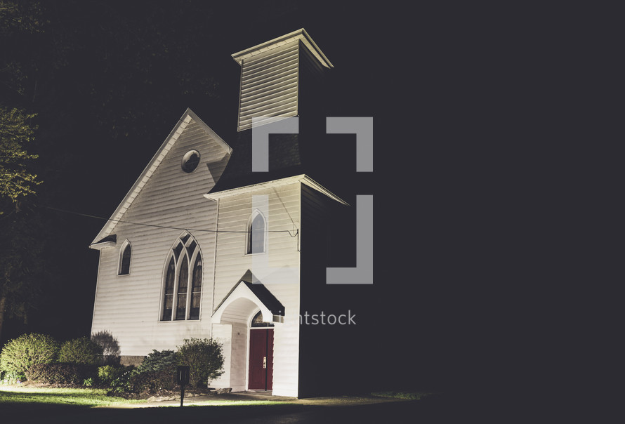 illuminated white church with steeple at night 