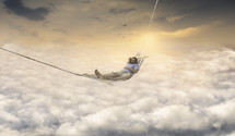 a man in a hammock relaxing above the clouds 