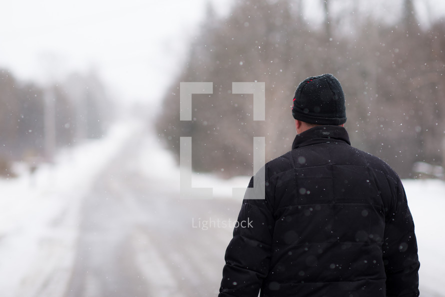 man standing in the middle of a road in falling snow 