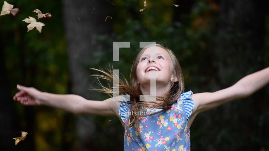 A little girl with arms outstretched watching in amazement autumn leaves fall 