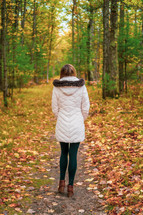 a woman walking on a path through a forest in fall 