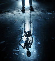 The figure of a skeleton forms in a puddle on a city sidewalk.