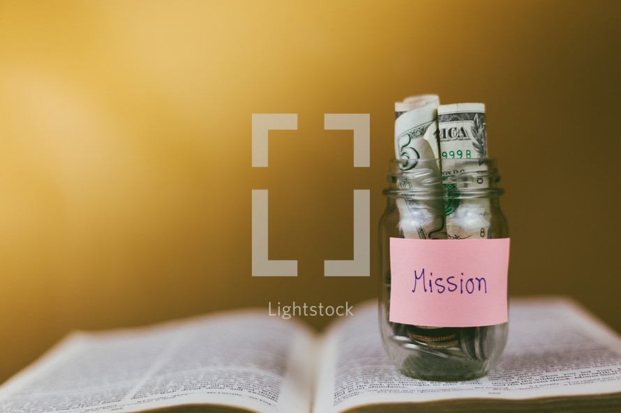 missions savings jar on the pages of a Bible 