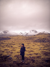 a woman standing outdoors with distant snow capped mountains in the background 