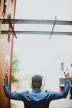 an African American man with raised hands standing in an alley 