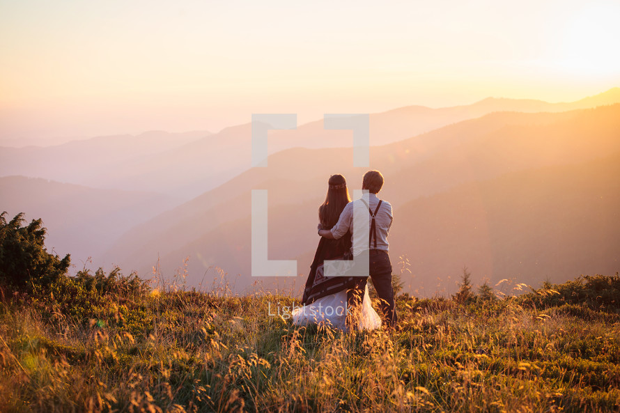 a bride and groom standing outdoors in a mountain landscape 