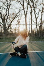 a woman sitting on a tennis court with sunlight in her hair 