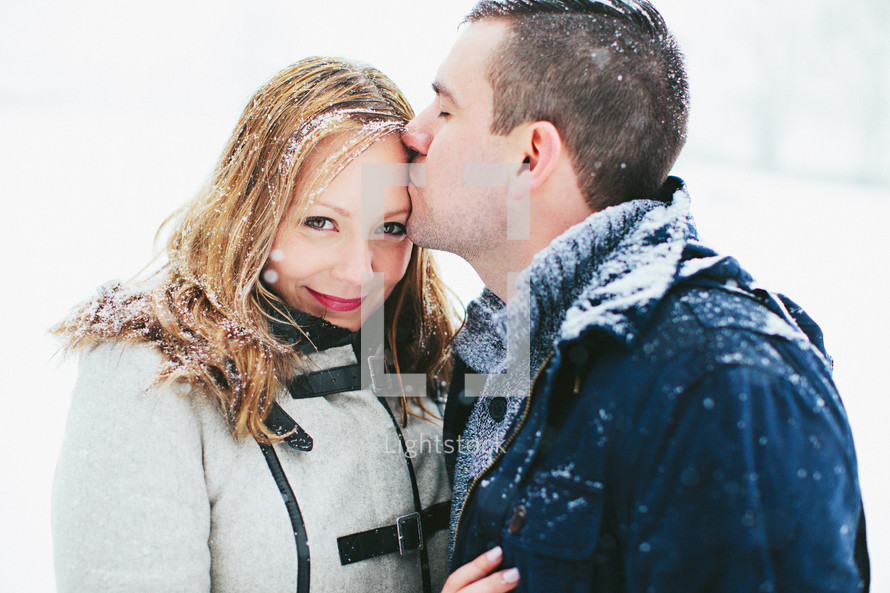 man kissing a woman on the forehead in the snow 